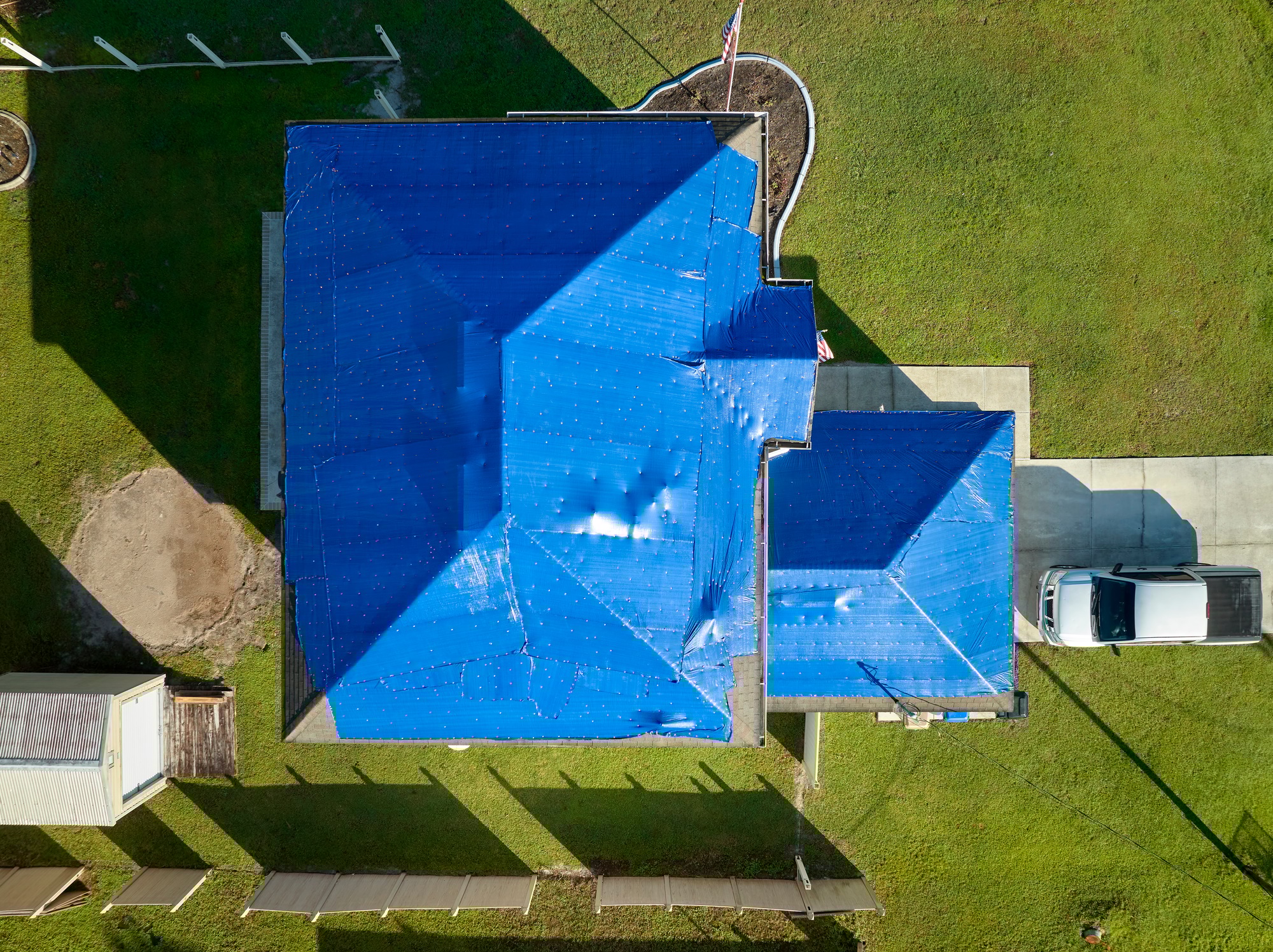 Aerial view of damaged in hurricane Ian house roof covered with blue protective tarp